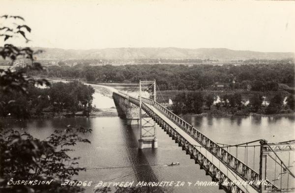 Elevated view of the bridge across the Mississippi River between Prairie du Chien, Wisconsin and Marquette, Iowa. Caption reads: "Suspension Bridge Between Marquette-IA & Prairie du Chien-Wis."