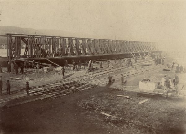 Slightly elevated view of the pontoon bridge construction. People are standing on and near the railroad tracks in the foreground.