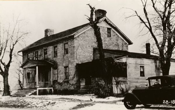 View of the front and right side of the Brisbois house. An automobile is parked on the right.