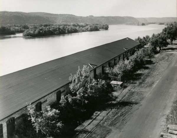 Elevated view over the long roof of the Diamond Jo warehouse. The Mississippi River is on the left, and hills are in the background.