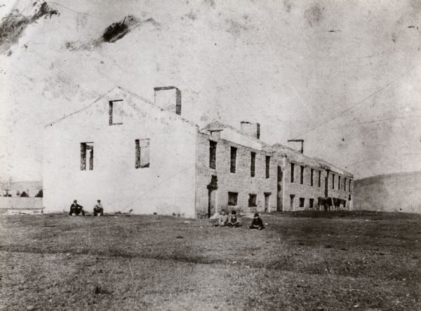 Fort Crawford ruins. This image may be even earlier than 1875; by the 1880's almost nothing was left of the actual fort compound buildings. Men are sitting on the ground near the building.