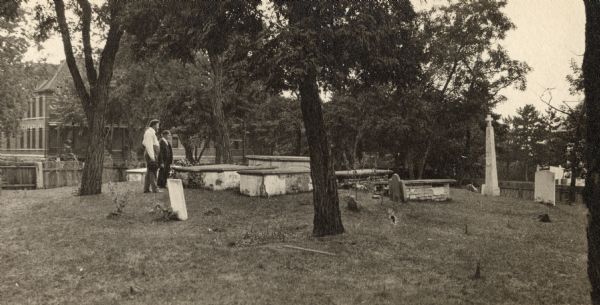 Fort Crawford Military Cemetery, as seen before it was restored by the United States Government. Two people are standing in the center near the tombs.