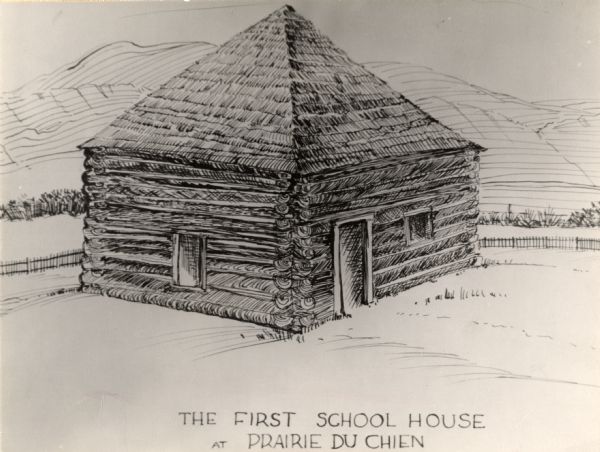The first school house at Prairie du Chien, Wisconsin. There is a fence behind the building, and hills in the background.