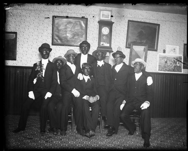 Eight men posing together dressed as minstrels in blackface makeup.