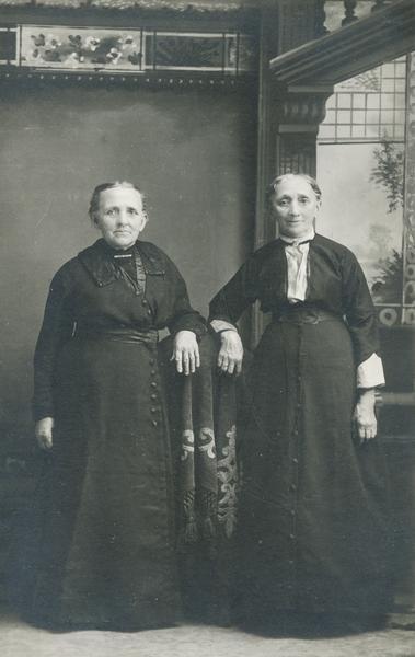 Studio portrait of the Yeatman sisters resting their arms on a piece of furniture in front of a painted backdrop.