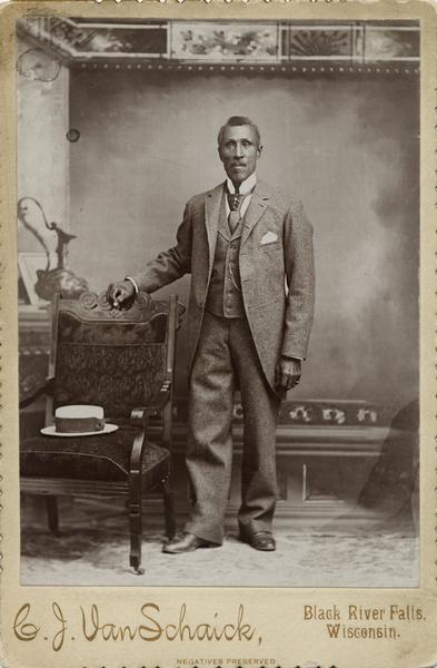 A studio portrait of Mr. William W. Hendricks, a Black River Falls barber, dressed in his best, posing in front of a painted backdrop.