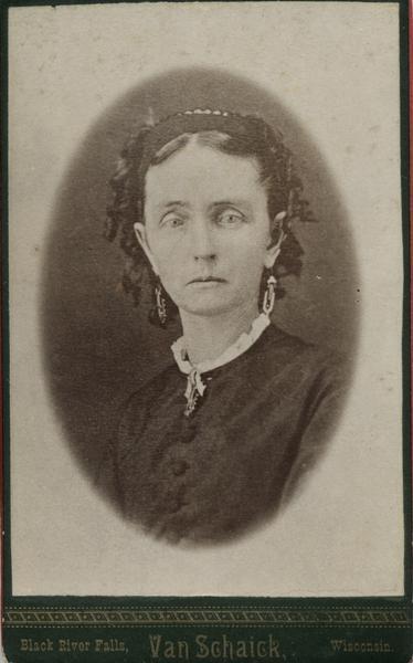 Oval quarter-length portrait of a young woman. She is wearing a band over her ringlet curls, a dark dress with buttons down the front, a short white lacy collar, and large dangling earrings and a brooch.  Although young looking, her eyes are cast downward and her mouth is pulled tightly downward.