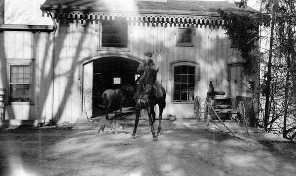 Belle Case La Follette on horseback in front of the barn at the Wisconsin Executive Residence on Gilman Street. This snapshot was taken during the period that her husband, Robert M. La Follette, Sr., was governor of Wisconsin.
