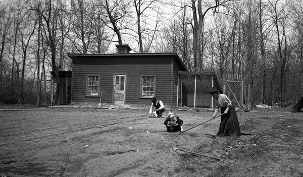 Belle Case La Follette hoeing the garden at Maple Bluff Farm in early spring. Two of her children are working with her, apparently planting seeds, and one of the farm buildings, perhaps a chicken house, can be seen in the background. It is likely that her husband, Senator Robert M. La Follette, Sr., was in Washington, D.C., at the time.