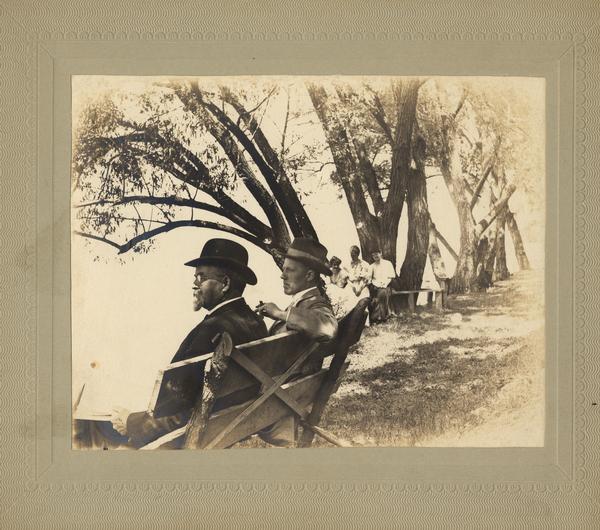 Attorney Albert G. Zimmerman (with cigar) and an unidentified man, enjoying the Lake Mendota breezes while seated on a rustic bench behind Zimmerman's lakeshore home at 746 East Gorham Street.  Zimmerman was a law partner of Robert M. La Follette, Sr., and later a judge.  According to local lore, the original property owner, William Leitch, grew the willow trees in the picture from cuttings from Napoleon's grave on St. Helena.