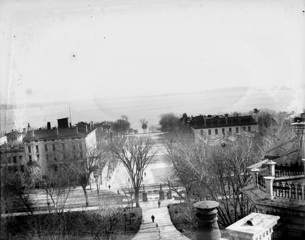 Attorney Albert G. Zimmerman took this photograph of Monona Avenue, with Lake Monona beyond, from the roof of the Madison Capitol about 1895.  Across Main Street from the Capitol are the Monona Hotel on the right and the Pioneer Block on the left.  Until 1894 Zimmerman was a law partner of Robert M. La Follette, Sr., in the firm La Follette, Harper, Roe, & Zimmerman that occupied offices in the Pioneer Block.  In that year, the partnership dissolved to allow La Follette to pursue his political career.  La Follette, Zimmerman, and Roe all moved down the street to adjoining, but independent offices in the Fairchild Block.  It is likely that Zimmerman took this photograph, as well as Image ID #30695 to document his two office locations.