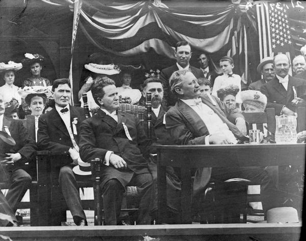 Seated at the table in front of the Wisconsin Building at the St. Louis World's Fair are Governor Robert M. La Follette, Sr., and Lieutenant Governor James O. Davidson.