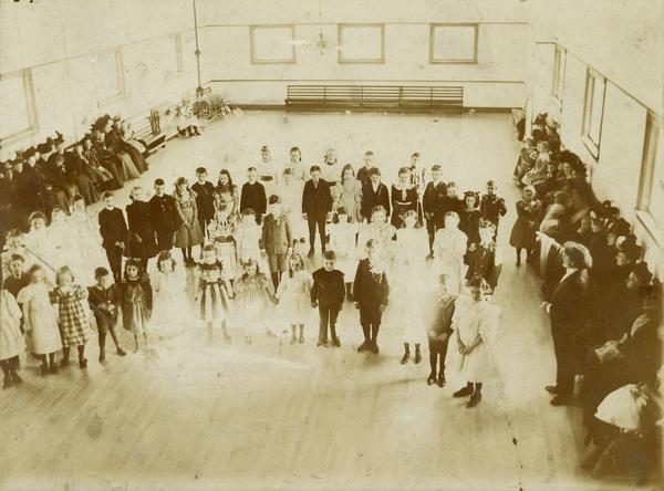 Dance class in the ballroom at the Kehl School of Dance, Madison, Wisconsin.  Professor Kehl stands at the lower right, while a row of mothers watch from both sides of the room.