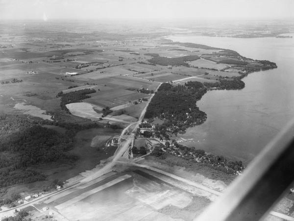 Aerial view looking northeast from a point over the east end of Middleton, showing the west end of Lake Mendota (right mid-ground). Fox Bluff juts into the lake (upper right mid-ground), and the north (bay) end of Lake Mendota, just right of the center background. In the lower center of the photo is the junction of Lake Street and a new road, the extension of Four Lake Drive, connecting Middleton and Westport. Just below and to the right of center in the photo is the Mendota Marina. In the background, just right of center, the Yahara River enters Lake Mendota. At the extreme right is Farwell's Point and Governor's Island.