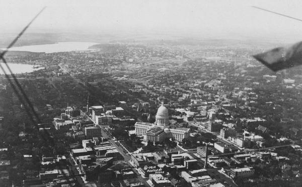 Aerial view with the Wisconsin State Capitol in the foreground, and the tip of Monona Bay and Lake Wingra to the left, with horizon stretching into the distance.