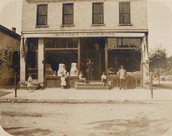 Group of people posing in front of the Reindl Brothers' Groceries and Provisions store at 32 North Bassett Street.