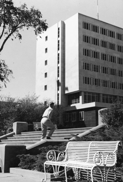 A man walks up the stairs leading to the City County Building. There is a bench in the foreground.