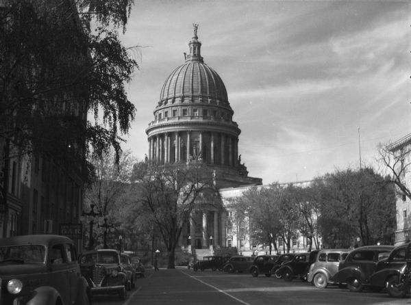 Exterior view of the Wisconsin State Capitol from Martin Luther King Boulevard. Cars are parked along the side of the street.
