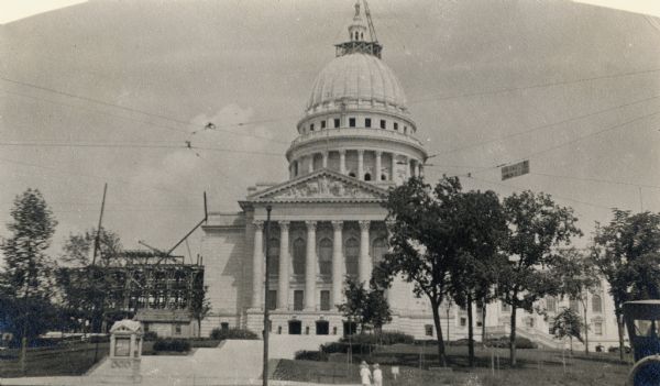 The Wisconsin State Capitol under construction during the summer of 1914. One wing is still under construction and the statue "Wisconsin," by Daniel Chester French, is being placed on top of the Capitol Dome.