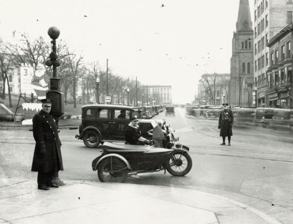 Two police officers, one on a motorcycle with sidecar on the corner of Mifflin and Carroll Street, on the Capitol Square.  A large Santa Claus cutout is located on the corner of the Square.