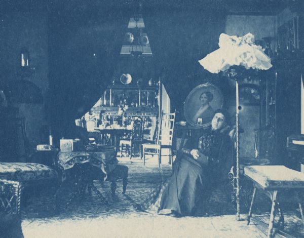 Cyanotype interior view of the Fairchild Residence, home of Lucius Fairchild. The woman sitting down is Mrs. Lucius Fairchild. Among the artworks that can be seen is a portrait of Sarah Fairchild Dean Conover, sister of Lucius Fairchild, painted by Eastman Johnson.