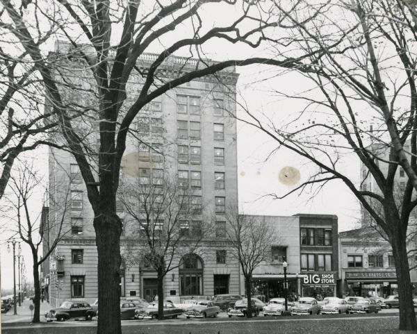 View from Capitol Park of the First National Bank building and other buildings on Pinckney Street. Cars are parked at an angle on the street.