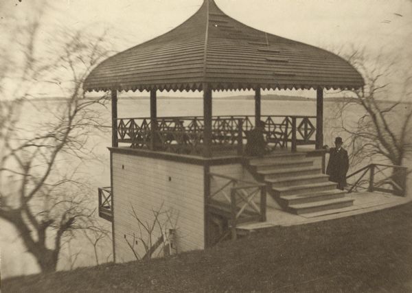 The Lucien S. Hanks boathouse at 216 Langdon Street. A man is standing on the right next to the steps that lead up to the pavilion on top of the boathouse. Lake Mendota is in the background.