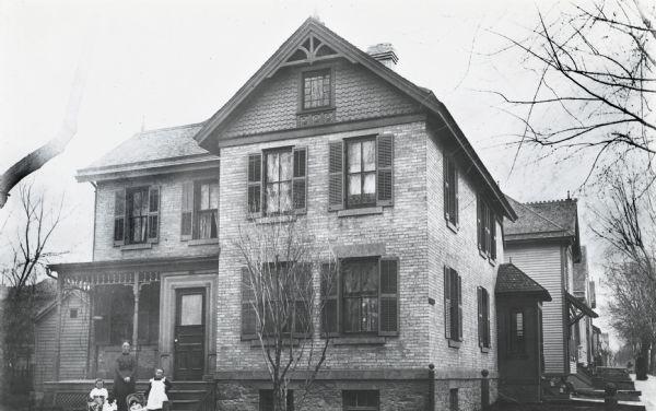 The William H. Holtzhauzen house, 351 West Washington Avenue. A group of people are posing near the entrance. Holtzhauzen, a German immigrant carpenter and builder, put up the two-story brick structure in 1868. The house was later owned by Mathias J. Hoven, a meat merchant, packer, livestock dealer, alderman, and mayor, who transferred the property to his son-in-law John Hartmeyer. Hartmeyer continued ownership of the property until 1947. The house was demolished in 1980 to make way for the new Jackson Clinic building and parking ramp.