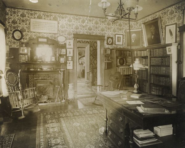 Interior of the Keyes residence, home of Elisha W. Keyes, political leader.  According to Keyes' daughter, Mrs. John C. Gaveney, the framed pictures, etc., above the bookcase, from door to the right, are: unknown, John C. Spooner, E.W. Keyes, Matthew Carpenter, a feather from the eagle "Old Abe," picked up by Keyes on the Capitol grounds from underneath the bird's perch. The motto framed and hanging above the fireplace reads: "I expect to pass through this world but once. Any good thing, therefore, that I can do, or any kindness I can show to any fellow human being, let me do it now. Let me not defer or neglect it, for I shall not pass this way again."