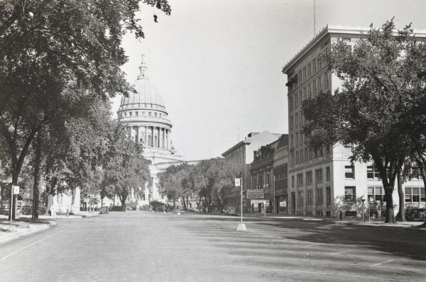 View up Monona Avenue towards the Wisconsin State Capitol. A marquee on the Madison Theatre on the right reads: "Test Pilot, Gable, Loy, Tracy" and "Extortion." The building on the right corner is "The Insurance Building."