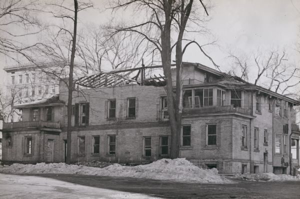 A rear view of the Atwood / Buck-Neckerman house, at 210-214 Monona Avenue (now Martin Luther King, Jr. Boulevard). Built by David Atwood and his partner Royal Buck as a double house in the 1840s. Caption reads: "Although many obvious alterations had been made in the house, it is the writers belief that the original house was considerably smaller than the house shown here. This is apparent from the interior structural details laid bare during the razing. It is impossible to say just what constituted the original building. The Insurance building is in the background."