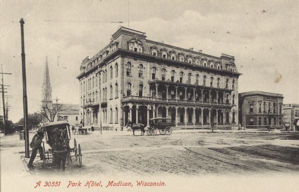 View across Main Street towards the Park Hotel on a corner. A church is behind the hotel on the left. In the left foreground a man is entering a horse-drawn buggy. Caption reads: "Park Hotel, Madison, Wisconsin.
