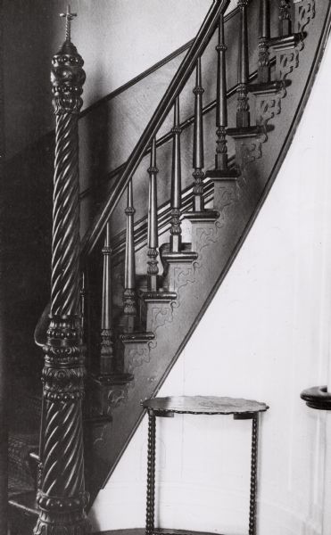 Interior view of the Pierce house at 424 North Pinckney Street. The stairway was built by A.D. Frederickson. The spiral stairway has solid hand-turned rails and spindles. The newel posts are hand-carved and the pickets are mahogony. The stairwell has a stucco rosette on the ceiling at the top.