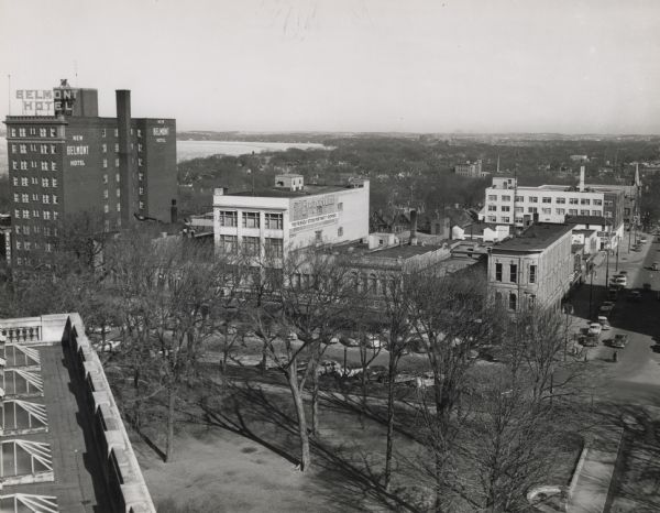 Elevated view of Pinckney Street, looking northeast from the Wisconsin State Capital. On the right is East Washington Avenue. On the left is the Belmont Hotel. A building near the Belmont Hotel has a sign painted on the side reading: "The Emporium. The Friendly Store for Thrifty Shoppers." In the far distance is Lake Mendota.