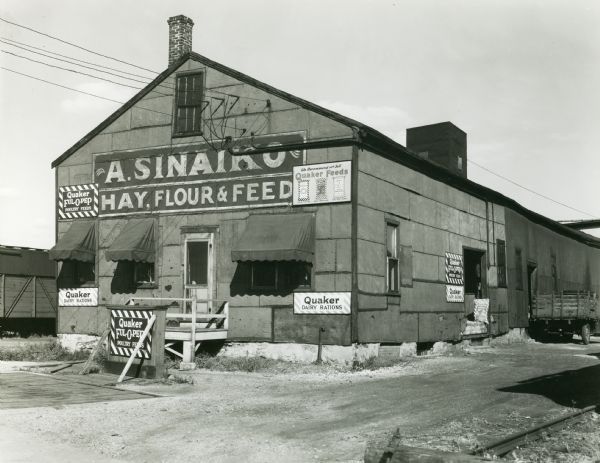 View of the A. Sinaiko Hay, Flour and Feed store, located at 653 West Washington Avenue. On the building are several advertisements for Quaker Feeds.