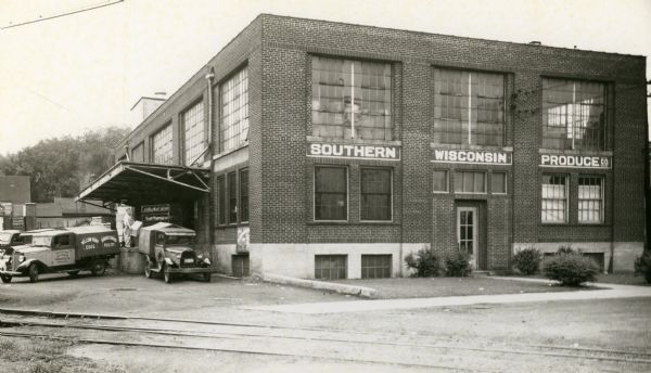 View of the Southern Wisconsin Produce building and its side loading dock, busy with orders. In addition, there are railroad tracks directly in front of the building.
