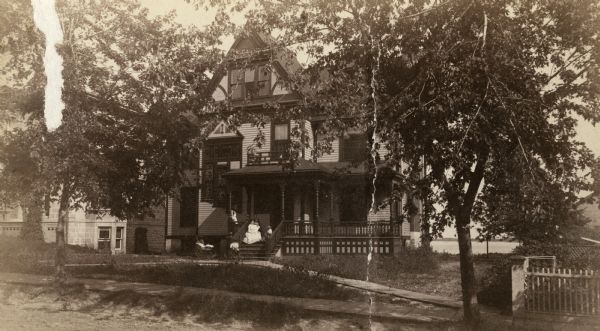 View of the Spooner residence on West Wilson Street. There are several children on the front porch of the home. Lake Monona is in the background.