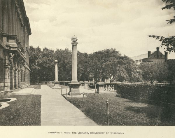 View along the front entrance of the Wisconsin Historical Society, across Library Mall towards the Armory (Red Gym or Old Red). Caption reads: "Gymnasium from the Library, University of Wisconsin."