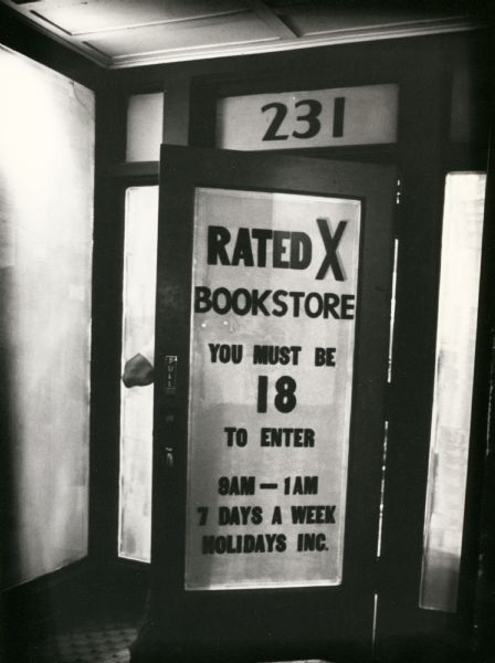 View of the doorway to Rated X Bookstore at 231 State Street. Part of a man's elbow is visible as he exits the store.