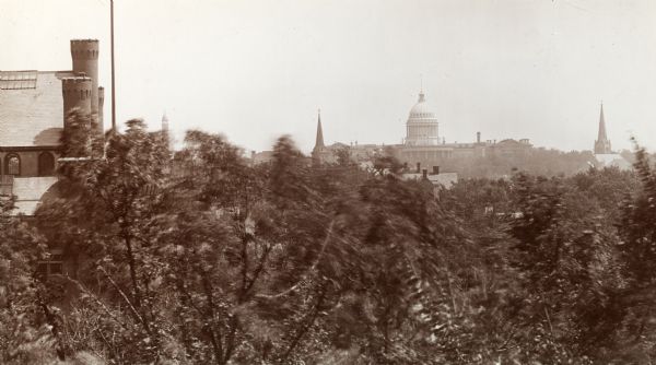 View of the Wisconsin State Capitol building from the above the treeline on the University of Wisconsin-Madison campus. On the left edge of the photograph the Armory (Red Gym or Old Red) is visible.