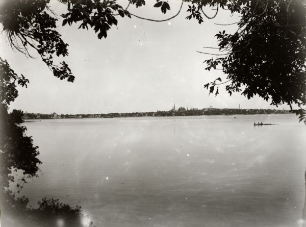 View across Lake Monoa towards Madison from the Old Assembly Grounds. Trees frame the view of the lake, and boaters are in the distance on the right.