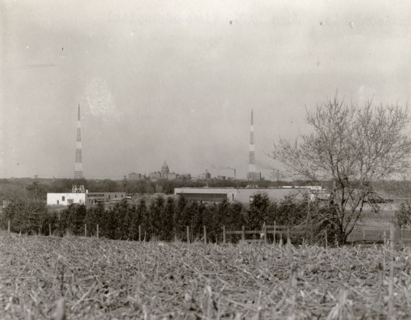 View towards the Wisconsin State Capitol from the outlying area around Madison. Just beyond the cornfield in the foreground are buildings, one with a sign for "Vita Plus Corporation". There are also two antenna towers.