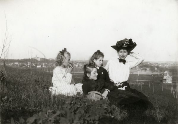 Four girls are sitting on a hill in University Heights. The city of Madison is in the background.