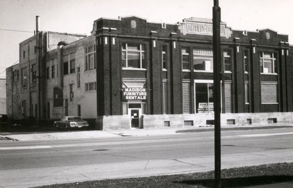 An exterior view of the Kennedy Dairy Company, which was built in 1910 and located at 621-629 West Washington Avenue. A sign above a doorway on the left side of the building reads: "Madison Furniture Rentals."