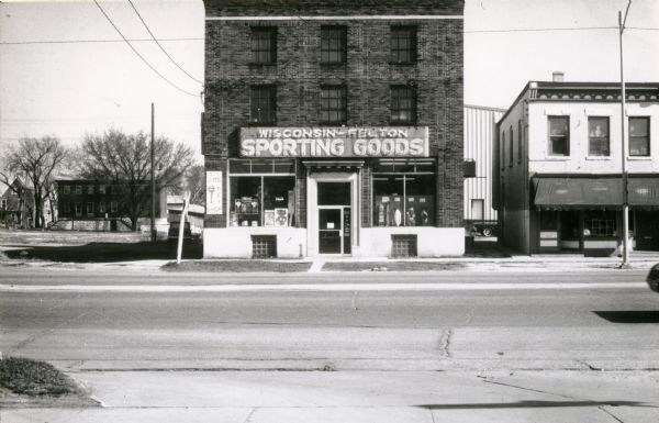 View of 615 West Washington Avenue, at the time of photograph, Wisconsin Felton Sporting Goods store. The adjacent lot once housed the Illinois Central passenger depot. In the background at 605 West Main Street, the Dorris (Doris?) House, also know as the Providence House is visible.