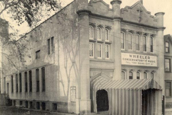 An exterior view of the Wheeler Conservatory of Music, located at 626 University Avenue. The entrance has a striped tent awning that extends out to the street over the sidewalk.