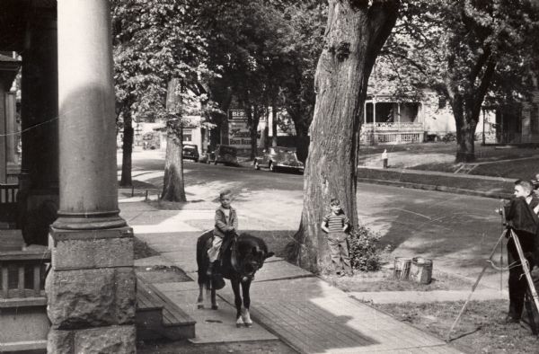 Billy Leiser posing for a photographer on a pony on the sidewalk outside of 1026 Williamson Street. In the background is Berkan's Grocery Store located at 1053 Williamson Street.
