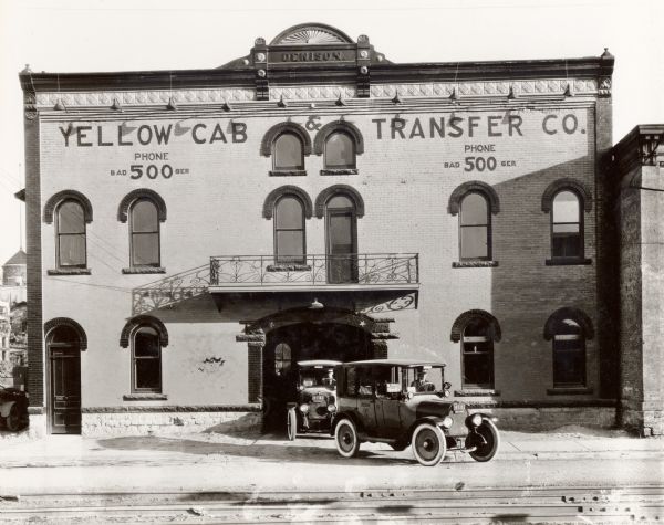 Exterior view of the Yellow Cab Transfer Company located at 643 E. Wilson Street, (housed in the Denison Building) with two cabs with drivers out front.
