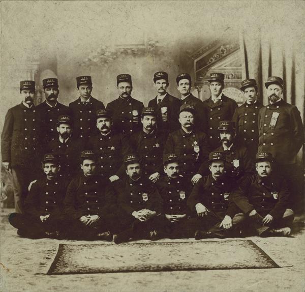 A group portrait of uniformed men, some with badges and ribbons, wearing hats that say "DHC, Mason City".