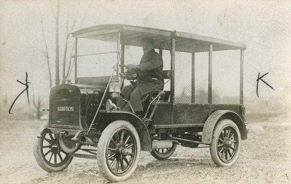 A man driving an early truck (ca. 1910). The front is labeled "Sampson".